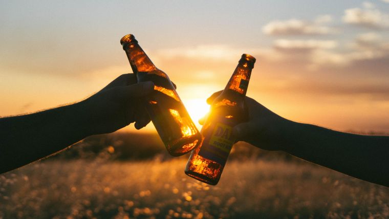 Image of two alcohol bottles being help up in front of a sunset.